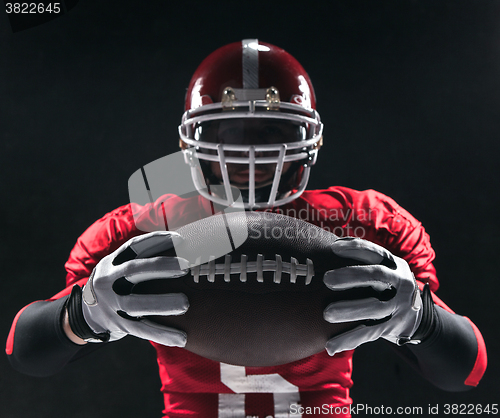 Image of American football player posing with ball on black background