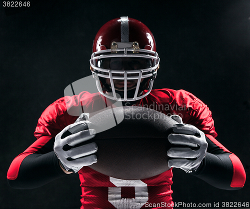 Image of American football player posing with ball on black background