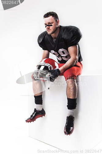 Image of American football player sitting with  helmet on white background