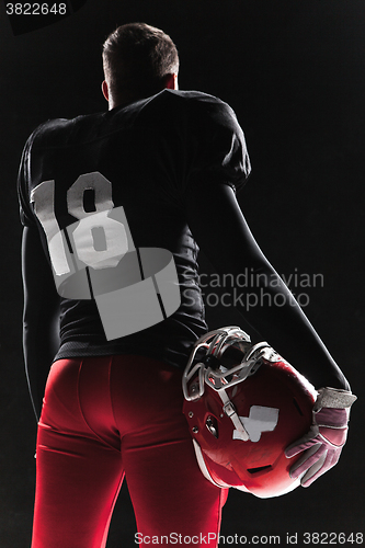 Image of American football player posing with ball on black background