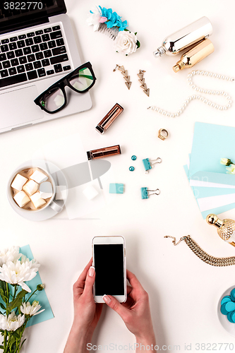 Image of The female hands and smart phone against blue objects on white