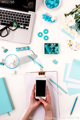 Image of The female hands and smart phone against blue objects on white