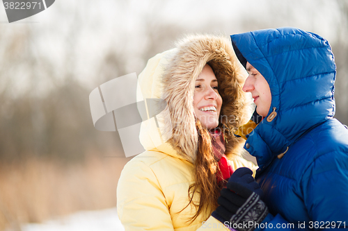 Image of happy pair of male and female embracing ain winter outdoors