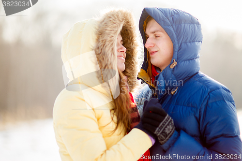 Image of happy pair of male and female embracing ain winter outdoors