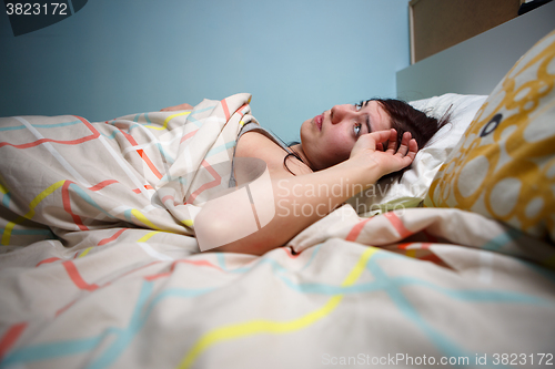 Image of Side view of a sleepy young woman suffering from headache with eyes closed in bed at home