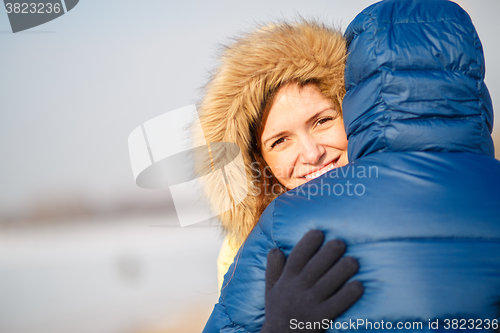 Image of happy pair of male and female embracing ain winter outdoors