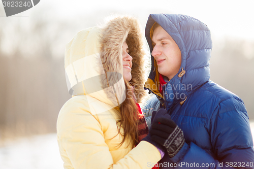 Image of happy pair of male and female embracing ain winter outdoors