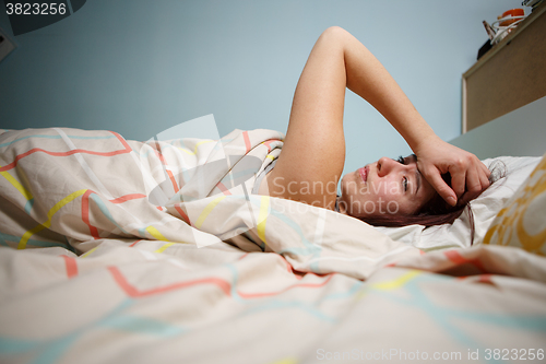 Image of Side view of a sleepy young woman suffering from headache with eyes closed in bed at home