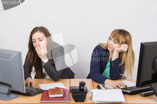 Image of Two young office employee wearily sitting behind a desk