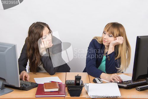 Image of Two young office employee wearily looking at each other behind a desk