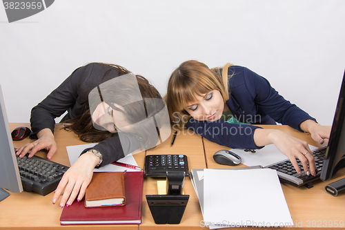 Image of Two young office employee asleep on desk for computers