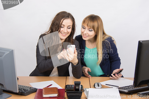 Image of Two branchless workers enthusiastically looking at cell phone at his desk