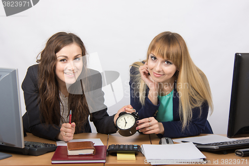 Image of Two girls in the office with the clock happily await the end of the working day