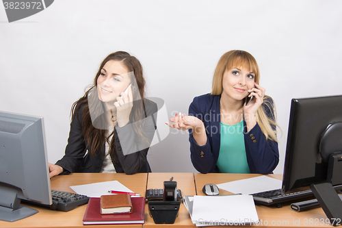 Image of Two girls at a desk talking on mobile phone in the office