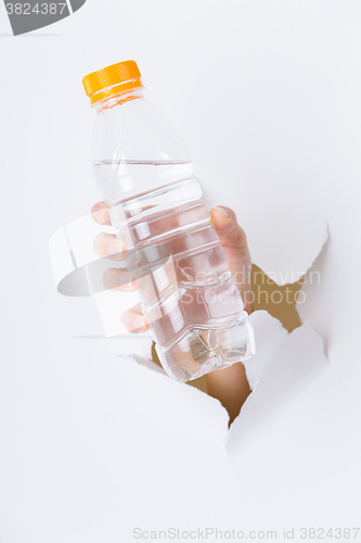 Image of Hand through the hole in paper with plastic bottle