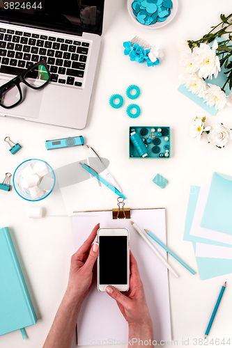 Image of The female hands and smart phone against blue objects on white