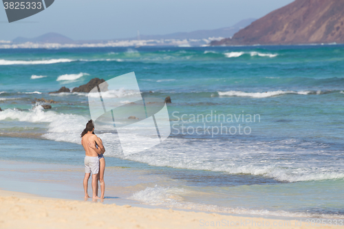 Image of Young couple embracing on sandy beach.
