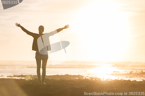 Image of Free woman enjoying freedom on beach at sunset.