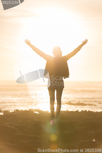 Image of Free woman enjoying freedom on beach at sunset.