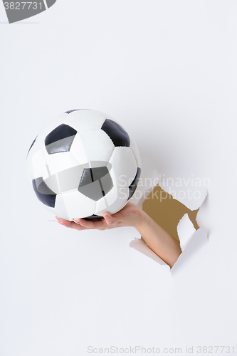 Image of Hand through the hole in paper with soccer ball