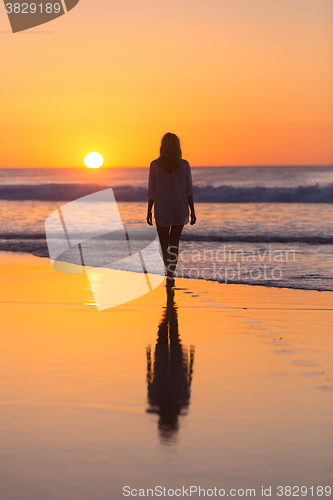 Image of Lady walking on sandy beach in sunset.