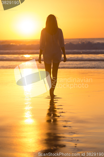 Image of Lady walking on sandy beach in sunset.