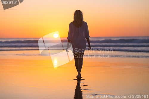 Image of Lady walking on sandy beach in sunset.