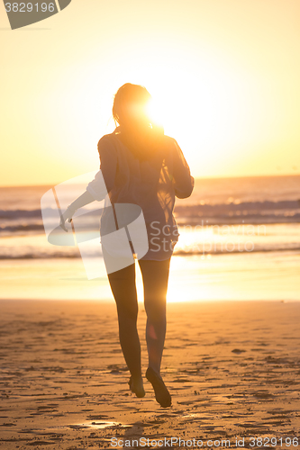 Image of Woman running on the beach in sunset.