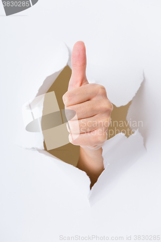 Image of Hand through the hole in paper with woman thumb up