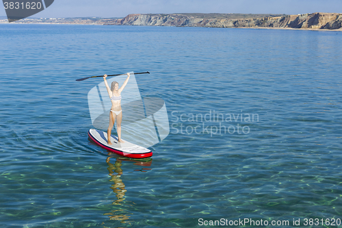 Image of A beautiful and happy woman with arms up and learning paddle-sur