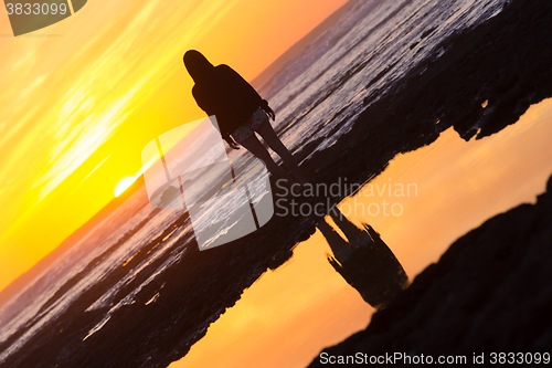 Image of Woman on rocky beach watching sunset.