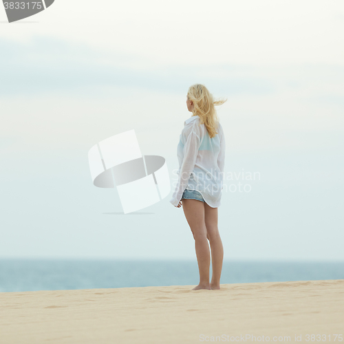 Image of Woman on sandy beach in white shirt at dusk. 