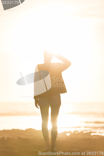 Image of Woman on sandy beach watching sunset.