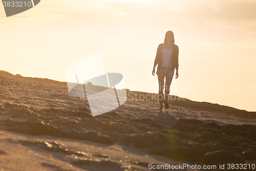 Image of Woman walking on rocky beach in sunset.