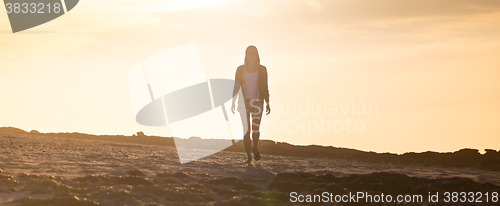 Image of Woman walking on rocky beach in sunset.