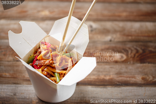 Image of Noodles with pork and vegetables in take-out box on wooden table