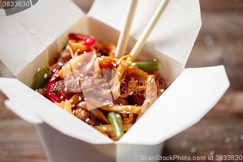 Image of Noodles with pork and vegetables in take-out box on wooden table