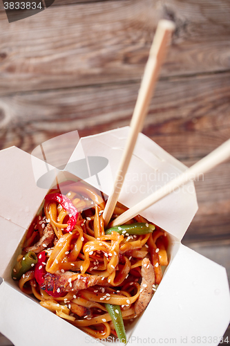Image of Noodles with pork and vegetables in take-out box on wooden table