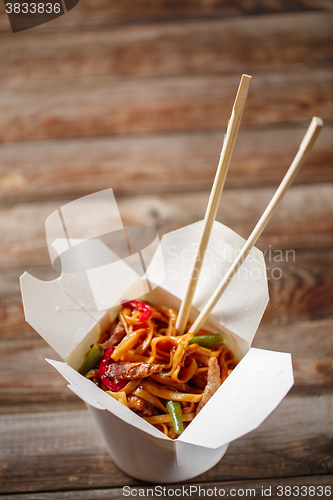 Image of Noodles with pork and vegetables in take-out box on wooden table