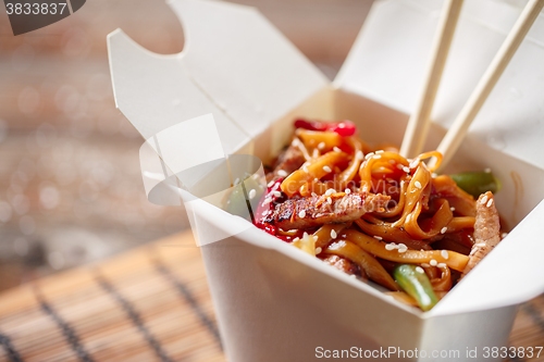 Image of Noodles with pork and vegetables in take-out box on wooden table