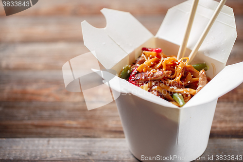 Image of Noodles with pork and vegetables in take-out box on wooden table