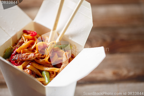 Image of Noodles with pork and vegetables in take-out box on wooden table