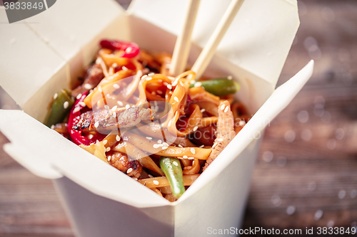 Image of Noodles with pork and vegetables in take-out box on wooden table