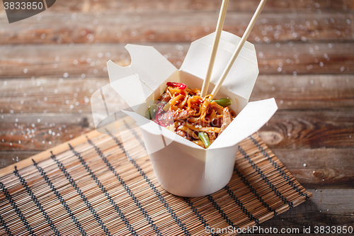 Image of Noodles with pork and vegetables in take-out box on wooden table