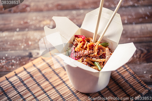 Image of Noodles with pork and vegetables in take-out box on wooden table