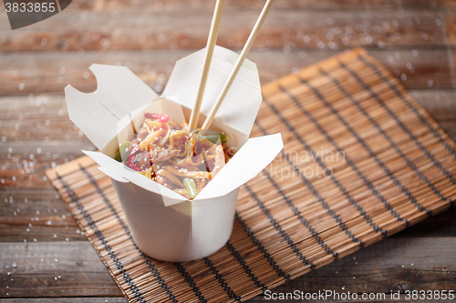 Image of Noodles with pork and vegetables in take-out box on wooden table