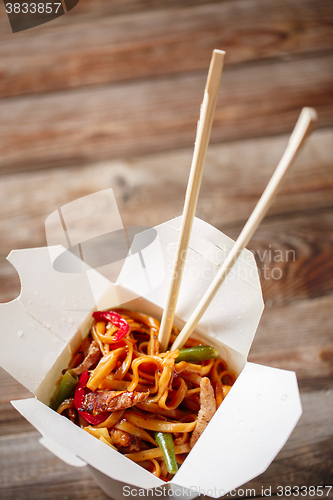 Image of Noodles with pork and vegetables in take-out box on wooden table