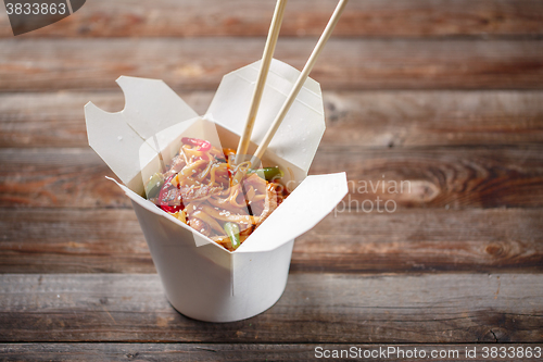 Image of Noodles with pork and vegetables in take-out box on wooden table