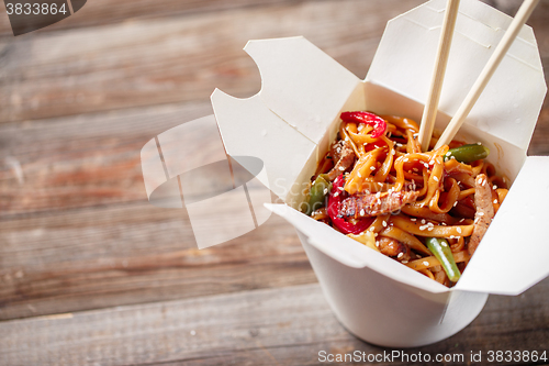 Image of Noodles with pork and vegetables in take-out box on wooden table