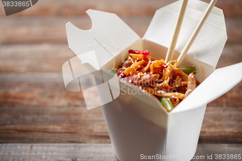 Image of Noodles with pork and vegetables in take-out box on wooden table